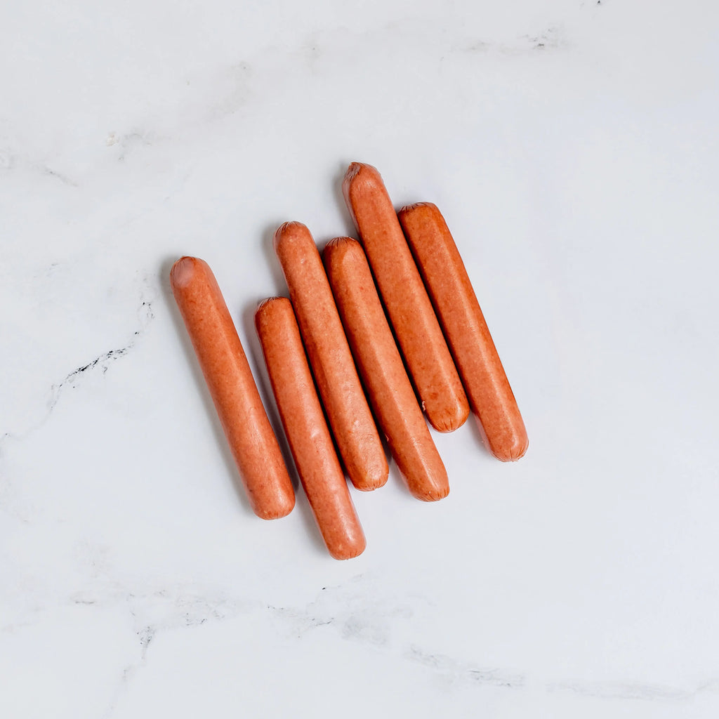 Six FREE Hot Dogs are arranged in a slightly fanned-out row on a white marble surface.